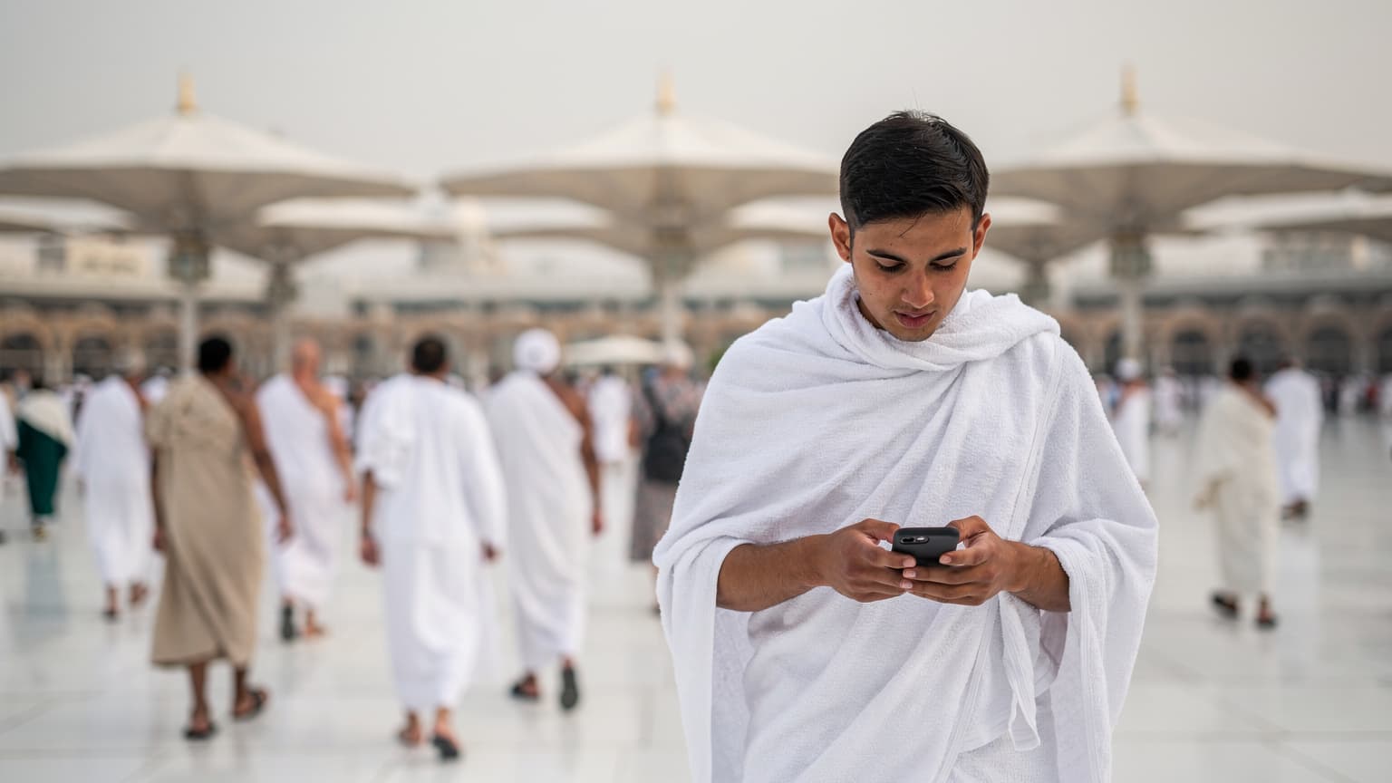 A diverse group of pilgrims walking towards the Prophet Mosque in Medina while one person checks their smartphone for directions.
