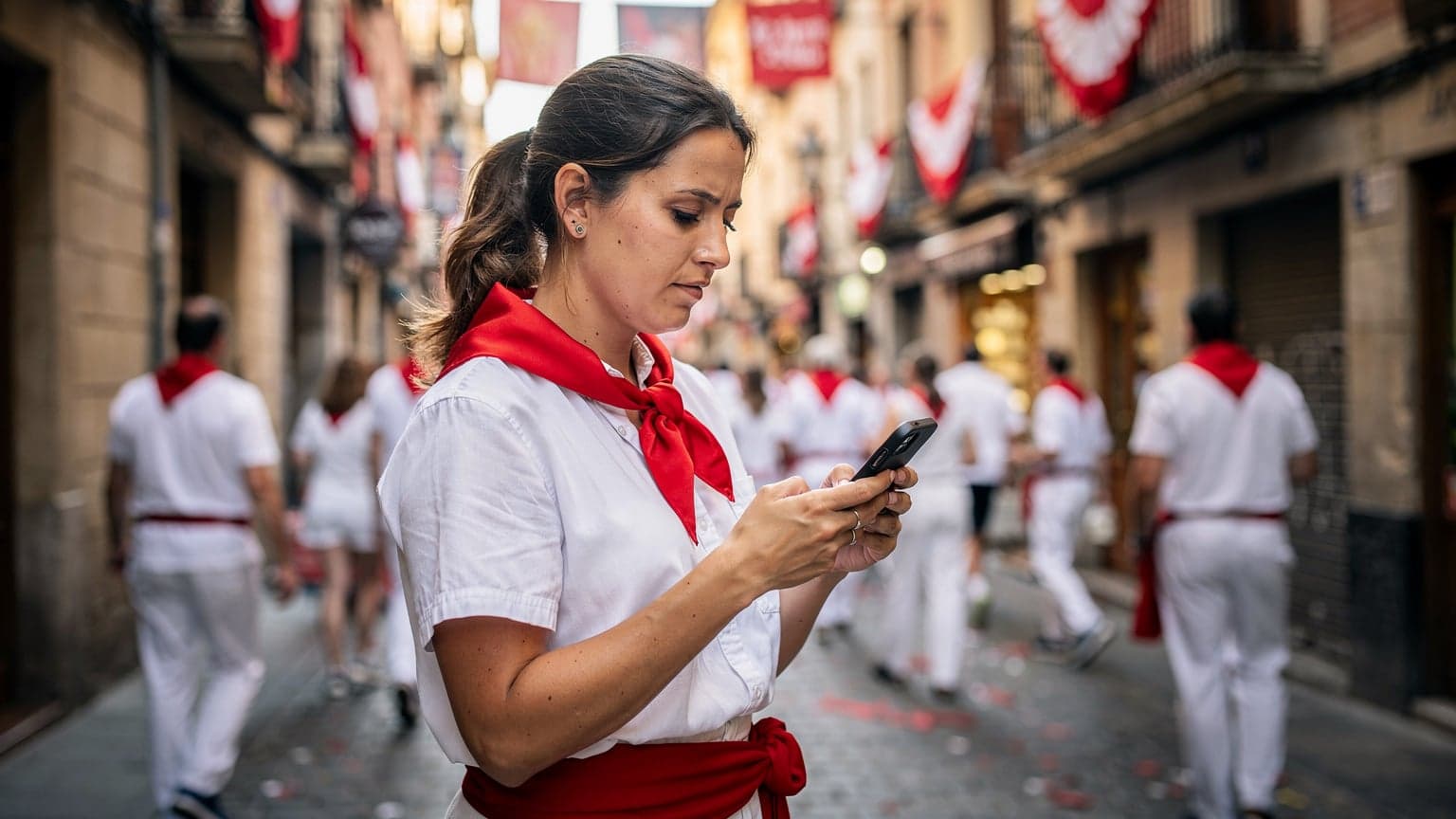A woman checking her phone for directions amidst a lively, crowded street in Pamplona during the San Fermín festival, with red and white festival attire visible.