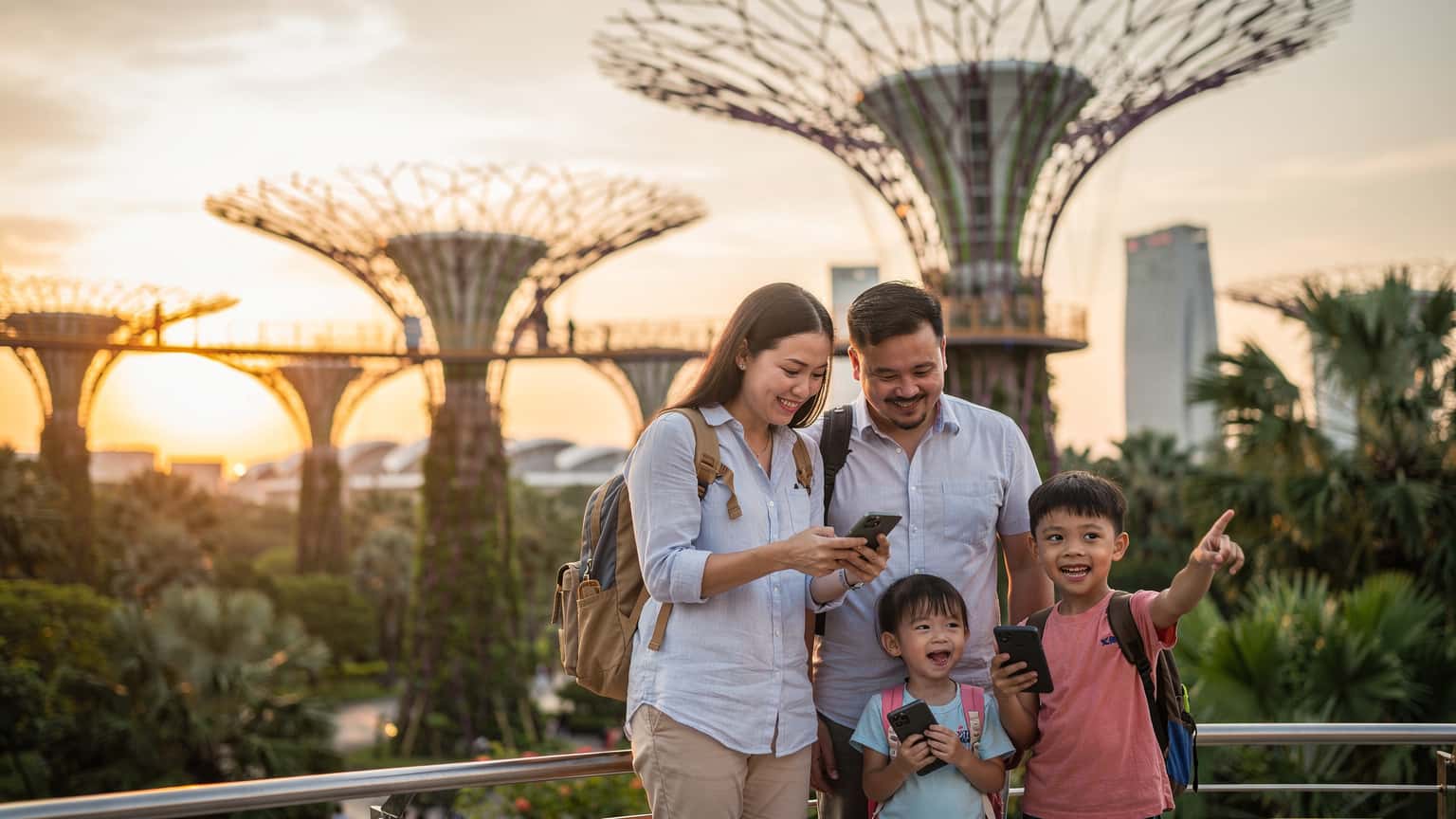 Một gia đình gồm bố mẹ và hai con nhỏ đang đi bộ qua Supertree Grove tại Gardens by the Bay, Singapore vào buổi tối, với những cây siêu cây phát sáng rực rỡ phía sau.