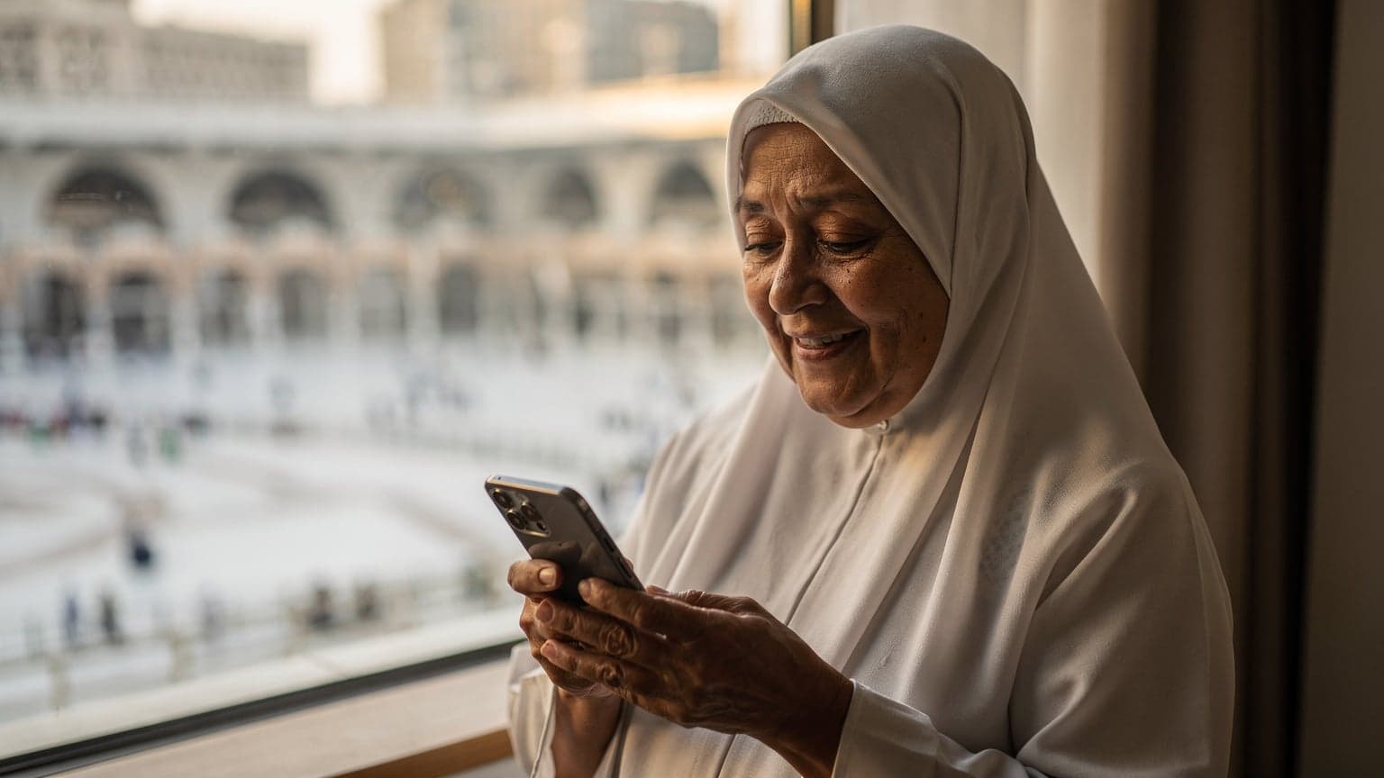 Seorang jemaah Malaysia yang lebih tua tersenyum sambil memegang telefon pintar dengan latar belakang Masjidil Haram di Mekah, menunjukkan kemudahan penggunaan eSIM untuk kekal berhubung.