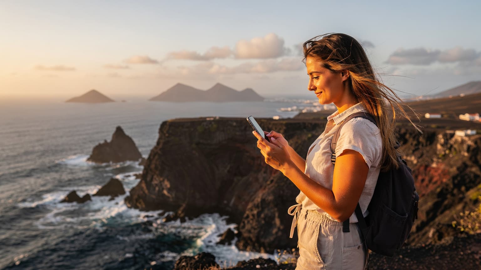 Uma pessoa utilizando um smartphone com um eSIM ativo, enquanto aprecia a vista panorâmica de uma praia de areia branca em Sal, Cabo Verde, sob um sol suave da manhã.