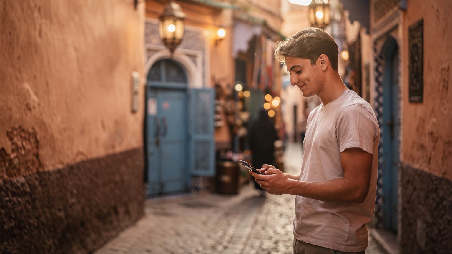 Een vrouw met een smartphone navigeert door de smalle, kleurrijke straatjes van de medina van Fes, Marokko, met traditionele Marokkaanse architectuur en handwerk op de achtergrond.
