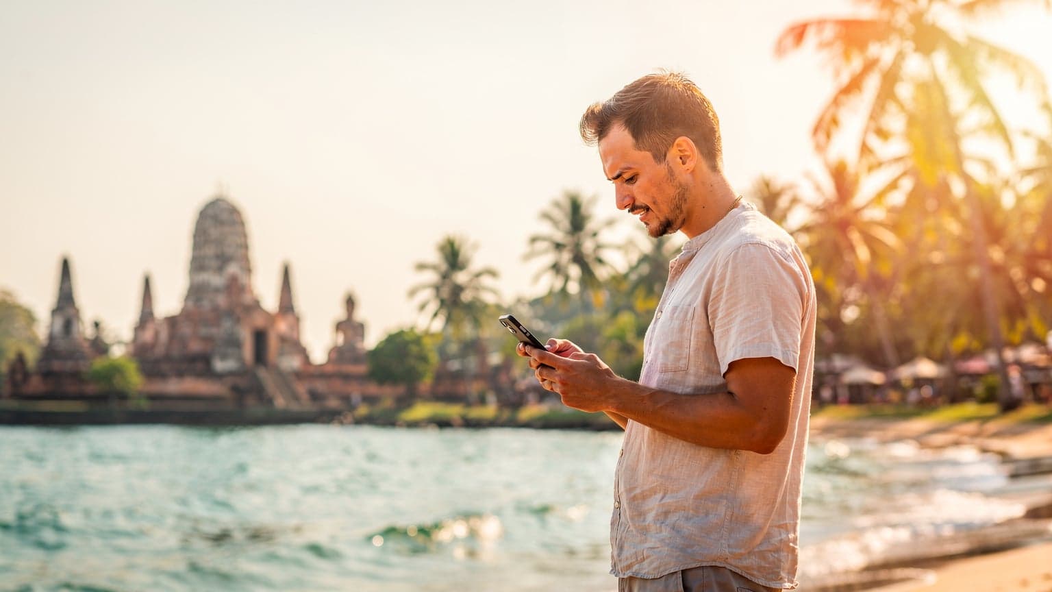 Une voyageuse naviguant sur son smartphone avec une eSIM active, assise sur une terrasse donnant sur le Wat Arun au coucher du soleil à Bangkok.