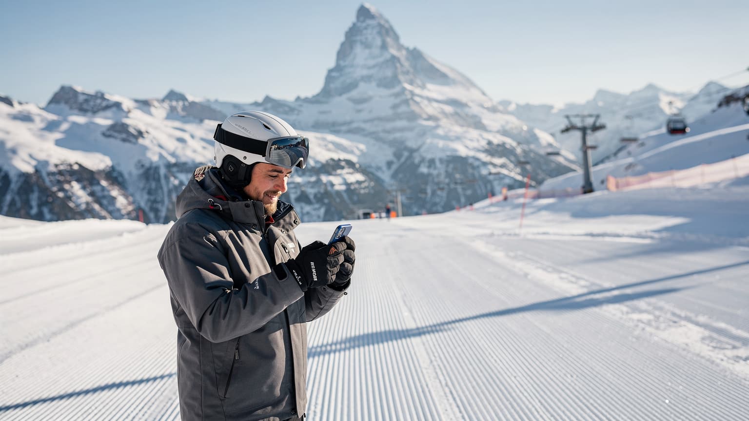 Eine Person auf einer Skipiste in den Schweizer Alpen, die ihr Smartphone überprüft, mit schneebedeckten Bergen im Hintergrund.