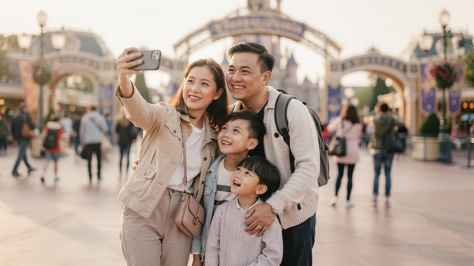 Một gia đình Việt đang mỉm cười chụp ảnh selfie trước cổng Disneyland Paris, người mẹ cầm điện thoại có hiển thị màn hình cài đặt eSIM, hai đứa trẻ 6 và 10 tuổi đang hào hứng nhìn vào camera.