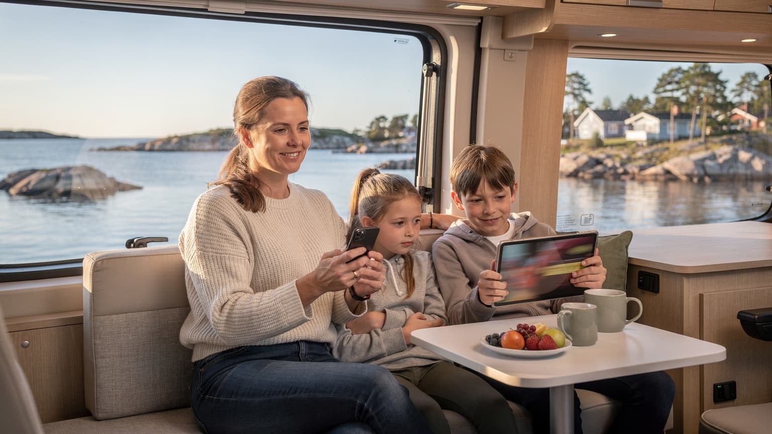 En mamma och hennes två barn (cirka 8 och 10 år gamla) sitter i en husbil i skärgården och tittar på en surfplatta medan mobilen är uppkopplad.