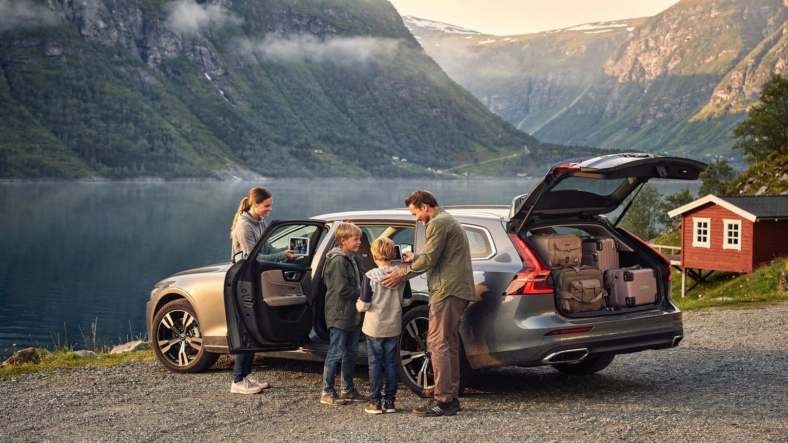 Een familie met twee kinderen pakt hun auto in voor een roadtrip met de majestueuze Noorse fjorden op de achtergrond, de zon schijnt zachtjes over het landschap.