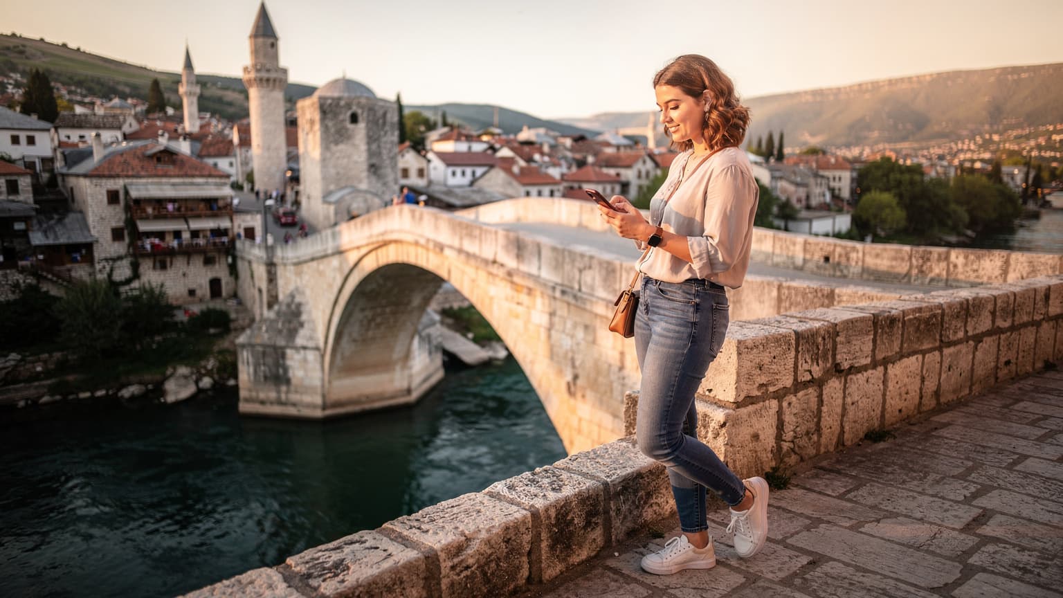 Bosna-Hersek'in Mostar şehrinde, Neretva Nehri üzerinde yükselen tarihi Mostar Köprüsü'nün üzerinde gün batımını izleyen genç bir kadın, telefonunda Cellesim uygulamasını kontrol ediyor.