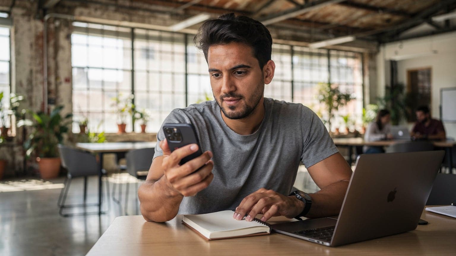 A seasoned digital nomad, mid-thirties, with a focused expression, holds an eSIM-compatible smartphone displaying a connectivity settings screen while seated at a communal wooden table in a bustling co-working space in Lisbon, Portugal, with a vintage-style espresso machine faintly visible in the background.