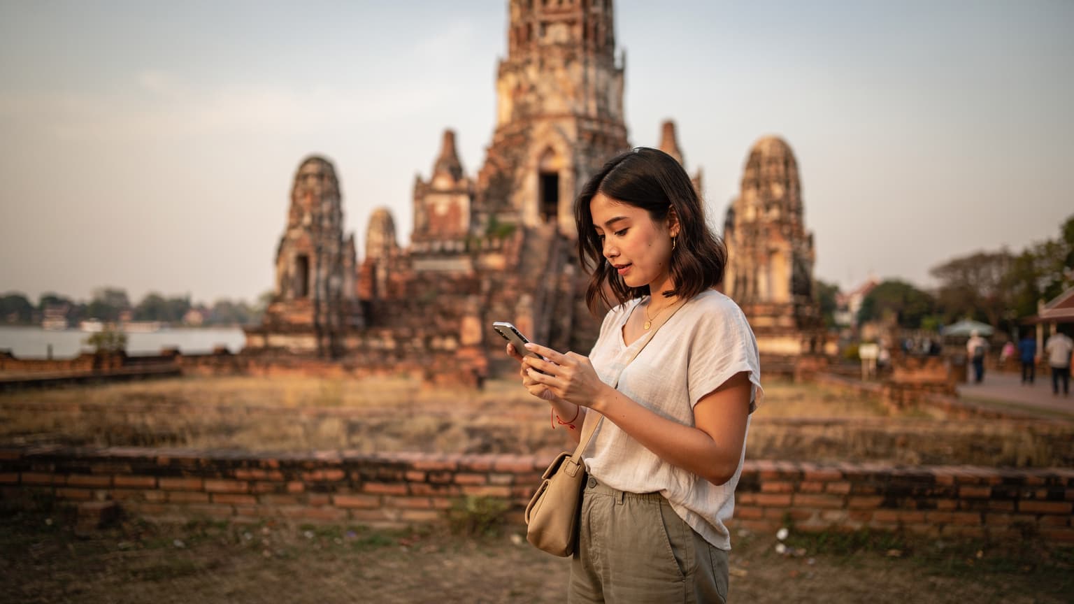 Une voyageuse naviguant sur son smartphone à l'extérieur d'un temple bouddhiste ancien et doré à Ayutthaya, Thaïlande, au lever du soleil.