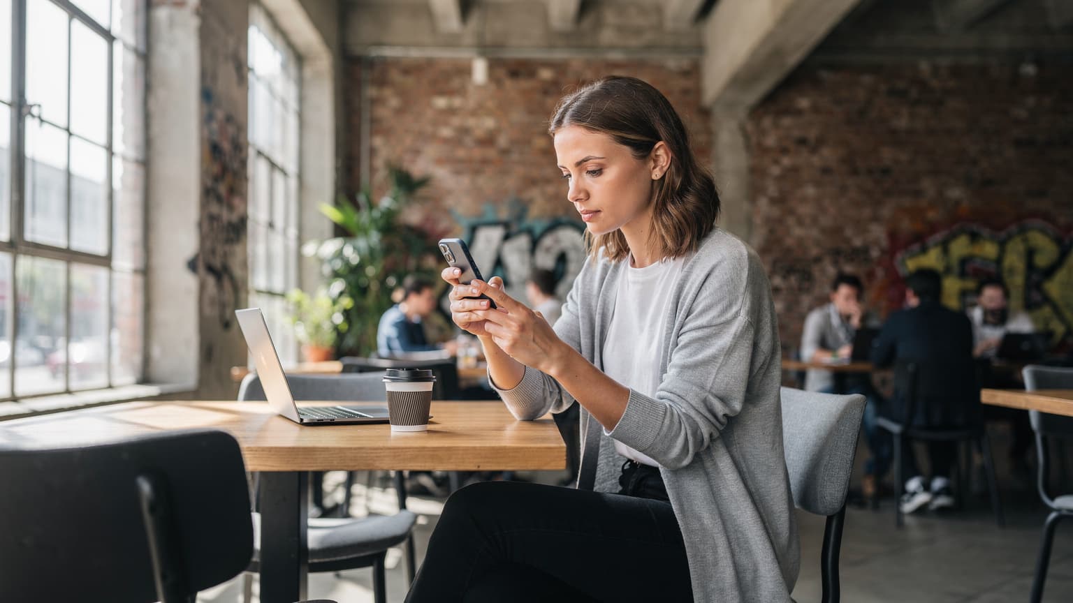 Eine junge Frau sitzt in einem belebten Co-Working-Space in Berlin-Kreuzberg, blickt auf ihr Smartphone und vergleicht eSIM-Tarife.