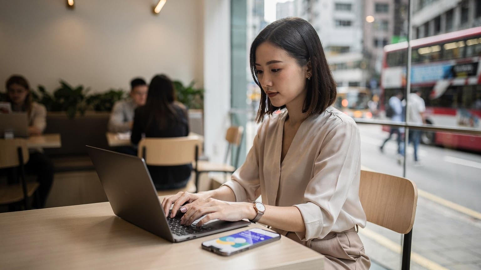 一名在香港中環 Coffeelin 咖啡館裡,專注使用筆記本電腦和手機的亞洲女性,窗外是繁忙的街道景觀。