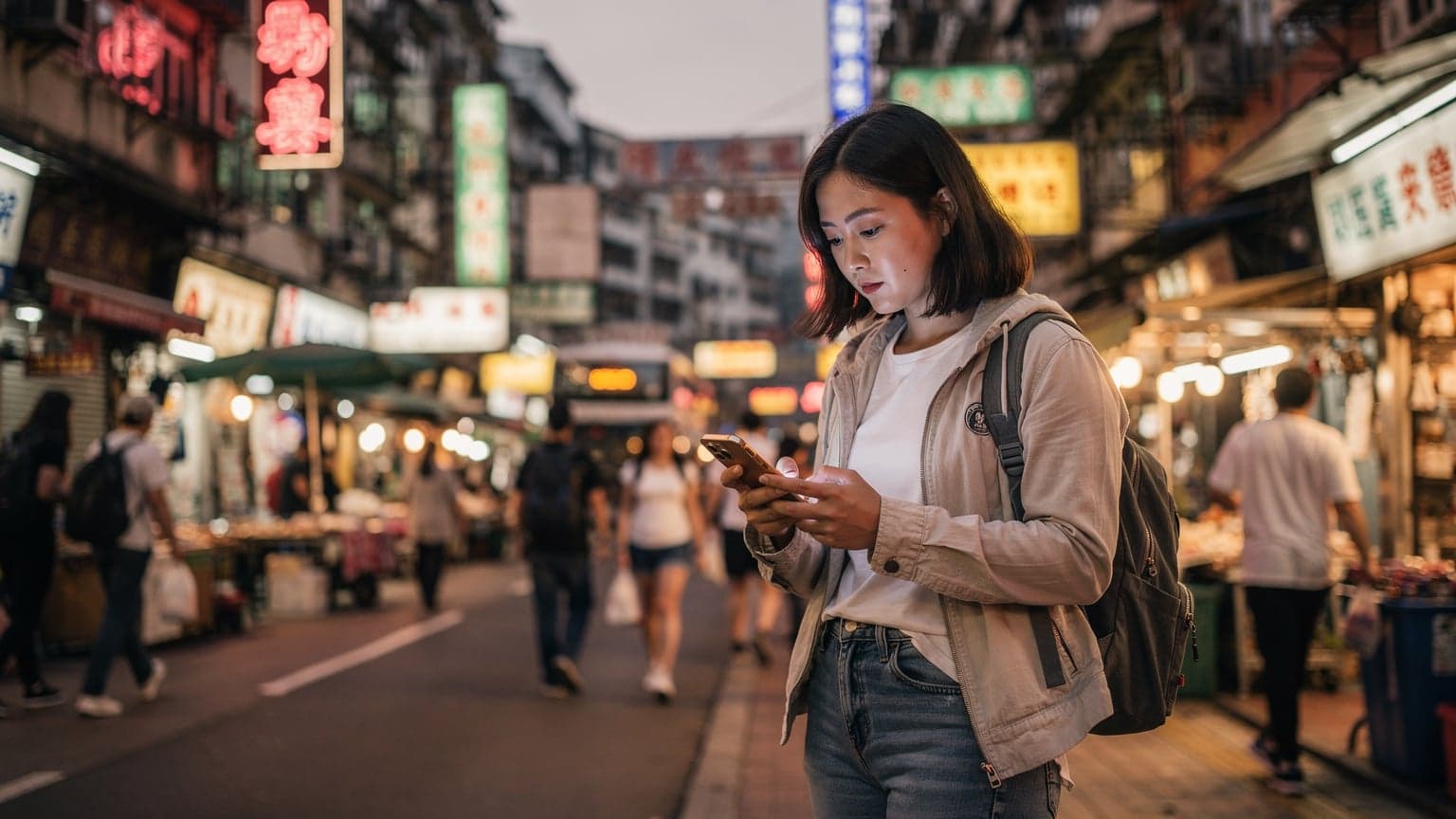 一名女性旅行者在香港旺角街頭手持iPhone查看地圖,背景是霓虹燈閃爍的繁忙街道。