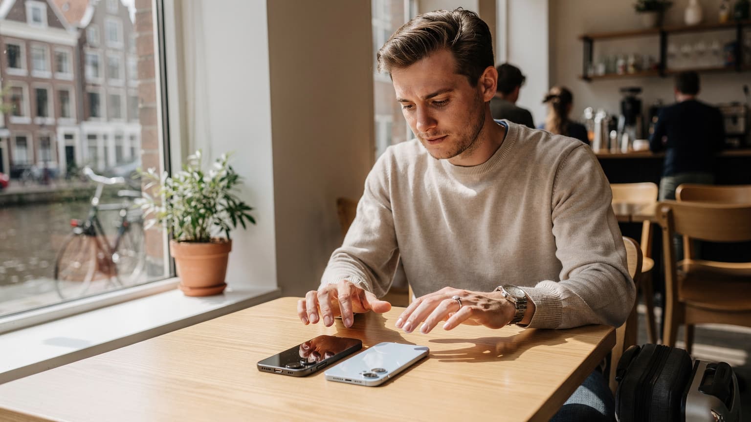 Een persoon in een modern café in Amsterdam met een nieuwe Samsung Galaxy S26 en een iPhone 17 op tafel, voorbereidingen treffend voor het overzetten van een eSIM.