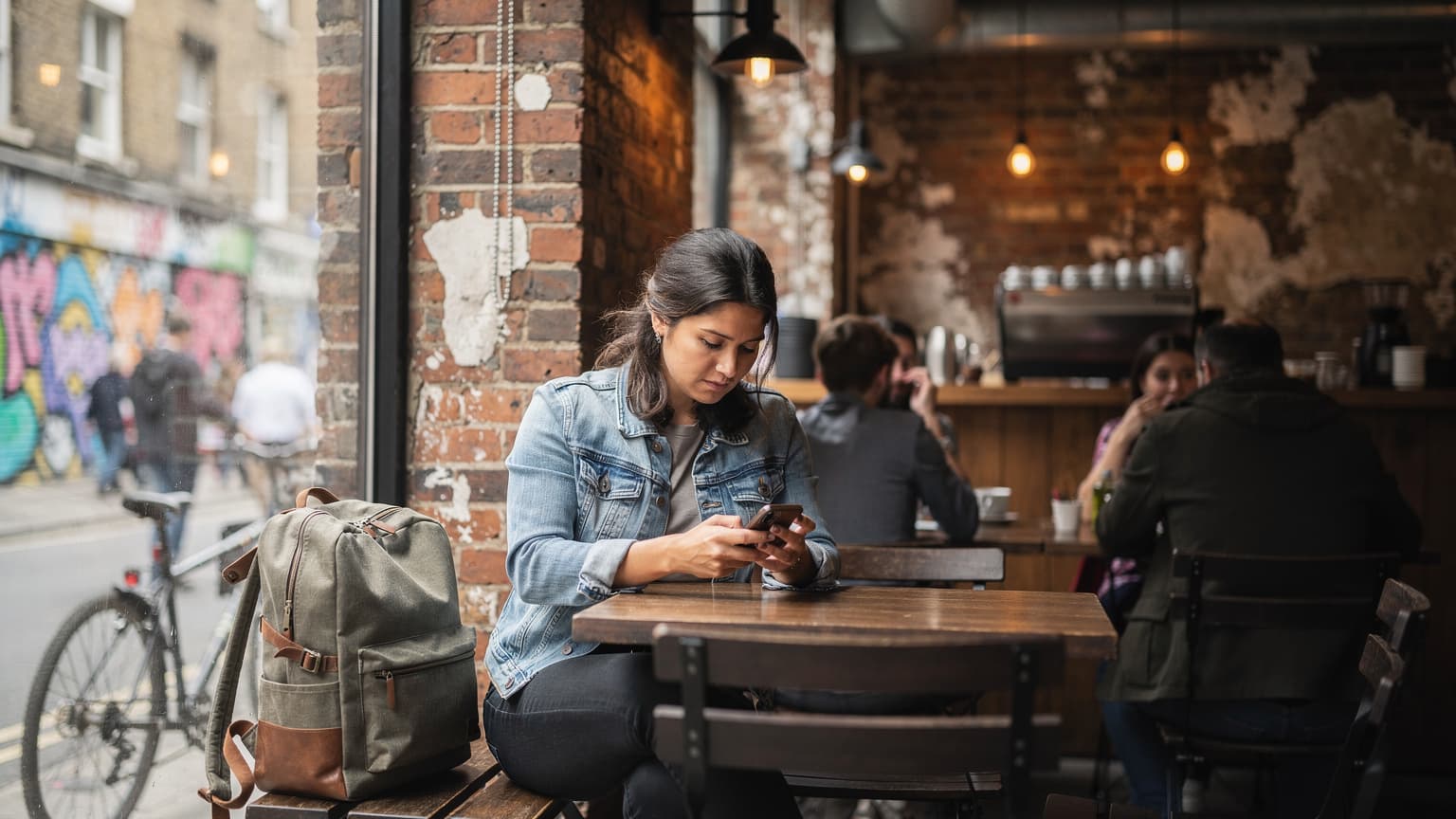 Londra'nın Shoreditch semtindeki canlı bir kafede oturan, elinde akıllı telefonuyla harita uygulamasını kontrol eden bir gezgin.