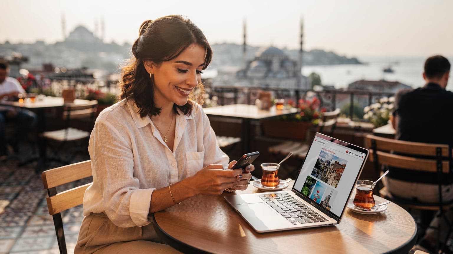 İstanbul'da tarihi yarımada manzaralı bir kafede, genç bir kadın dizüstü bilgisayarı ve akıllı telefonuyla eSIM kurulumu yaparken gülümsüyor.