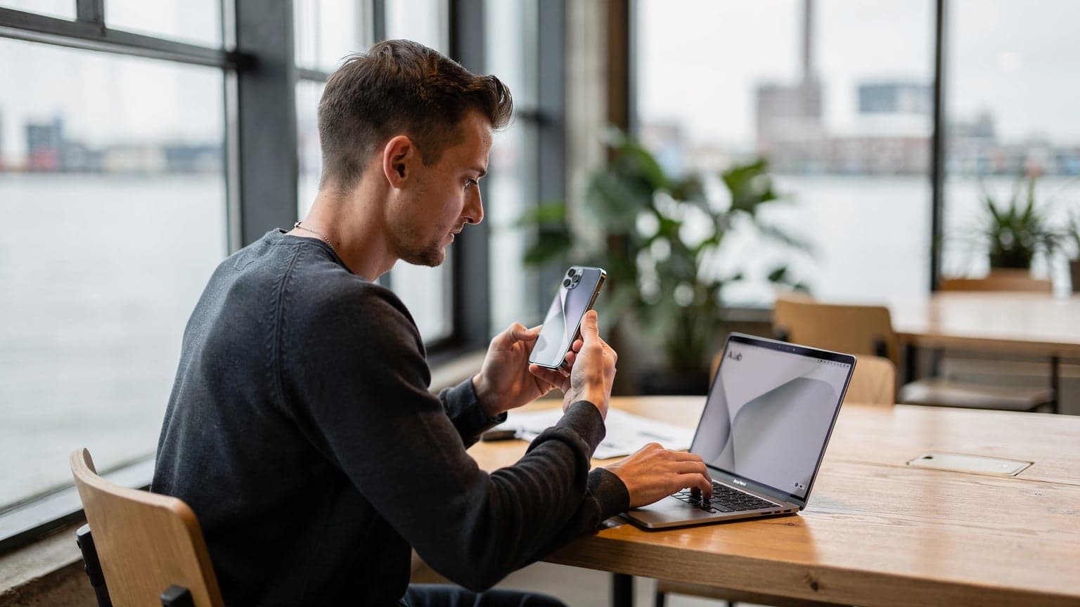 Een persoon zit geconcentreerd in een moderne co-working space in Amsterdam-Noord, met een nieuwe iPhone 18 en een laptop open, terwijl ze via een eSIM verbinding maken.