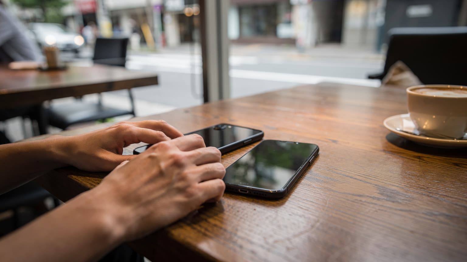 最新のiPhoneとAndroidスマートフォンが、開かれたパスポート、搭乗券、そして小さな地球儀の模型と共にカフェのテーブルに置かれている様子。
