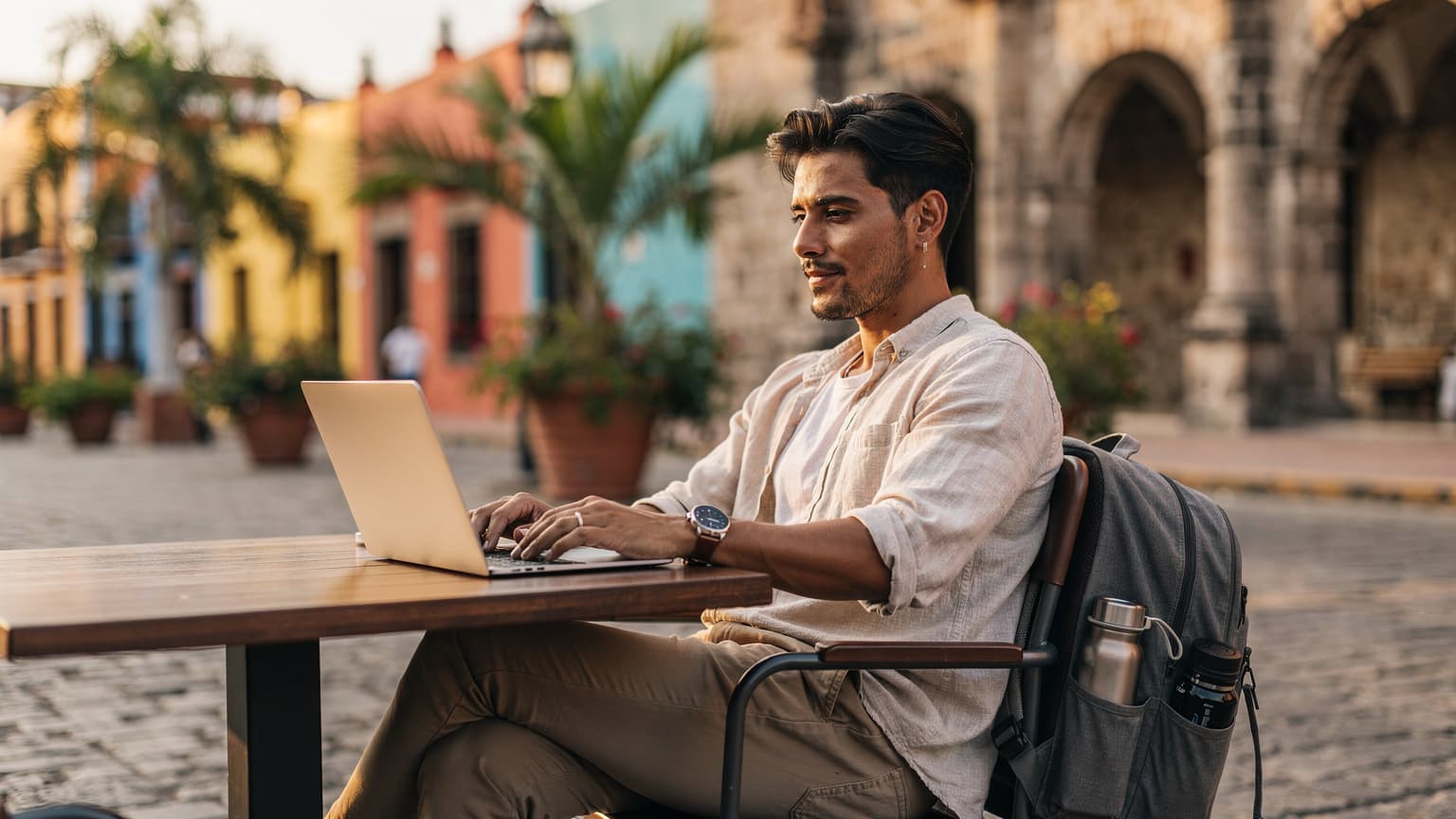 A diverse, modern digital nomad, likely in their late 20s or early 30s, is shown working on a laptop or tablet in an outdoor setting in Mexico. The background features a vibrant, authentic Mexican street scene with hints of traditional architecture. The person appears focused and prepared, with stylish travel gear subtly visible, conveying a sense of adventure, technology integration, and readiness for safe exploration. The image is a photorealistic, editorial travel magazine
