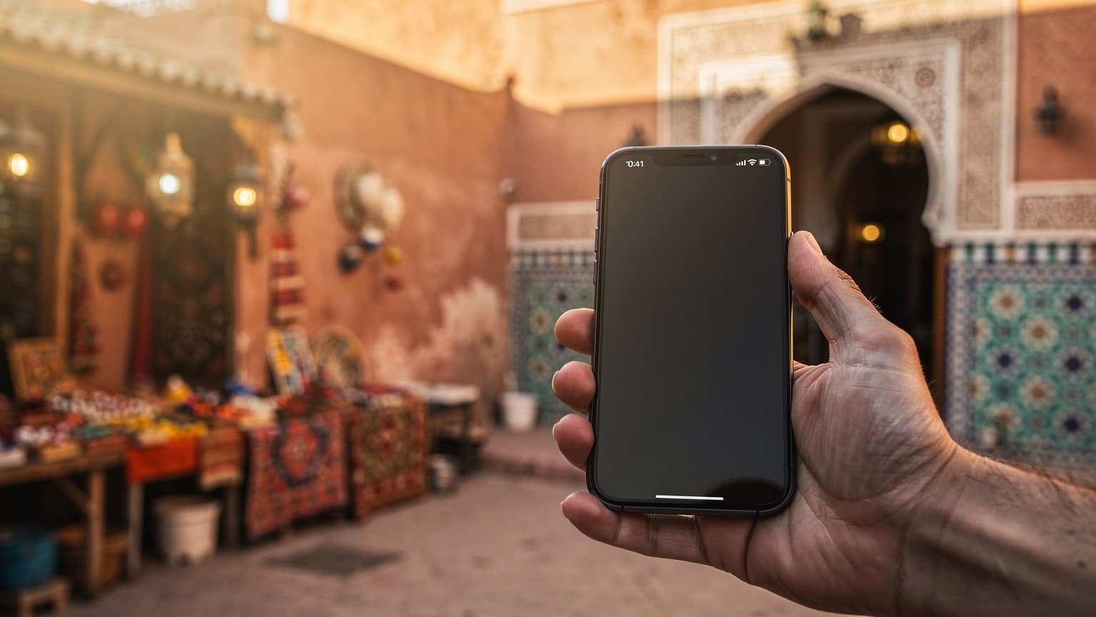 A close-up shot of a hand holding a modern smartphone in a blurred, sunlit Moroccan setting, representing digital connectivity choices for travelers.