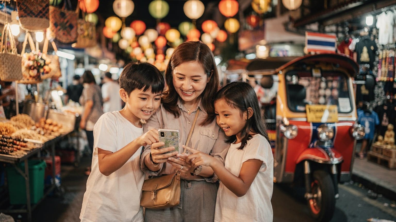 Seorang ibu dan dua anaknya tersenyum saat mereka melihat peta digital di ponsel di dekat sebuah tuk-tuk berwarna-warni di pasar malam di Bangkok, Thailand.