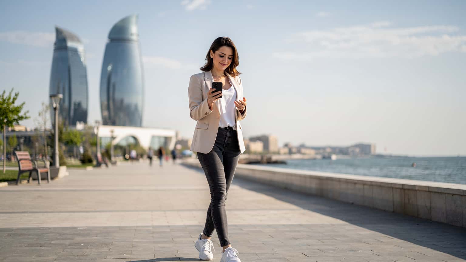 A woman confidently navigating the modern architecture of Baku, Azerbaijan, with a smartphone in hand, checking her eSIM connection.