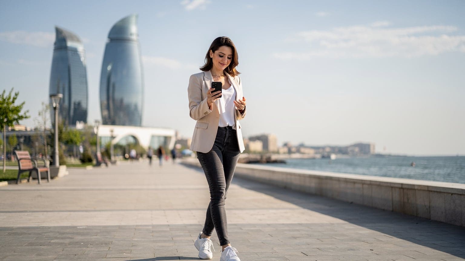 A woman confidently navigating the modern architecture of Baku, Azerbaijan, with a smartphone in hand, checking her eSIM connection.