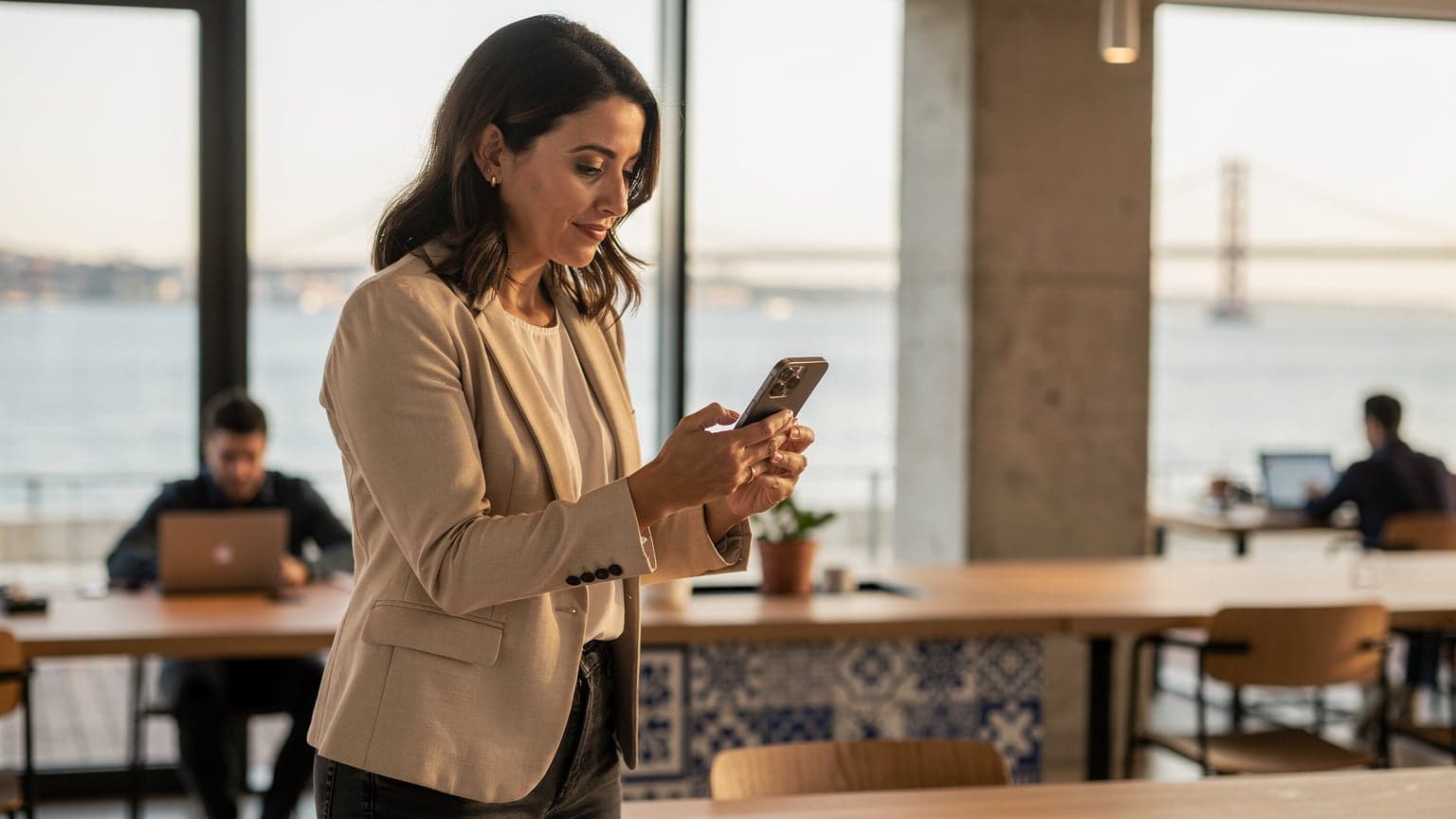 A woman using her iPhone to scan an eSIM QR code at a brightly lit co-working space in Lisbon, with traditional Portuguese tiles visible in the background.