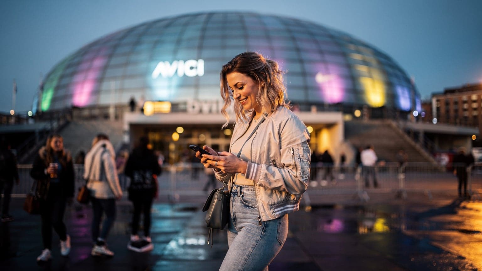 En person står framför ett upplyst Globen, nu Avicii Arena, i Stockholm under en konsertkväll i augusti, tittar på sin smartphone med ett leende.