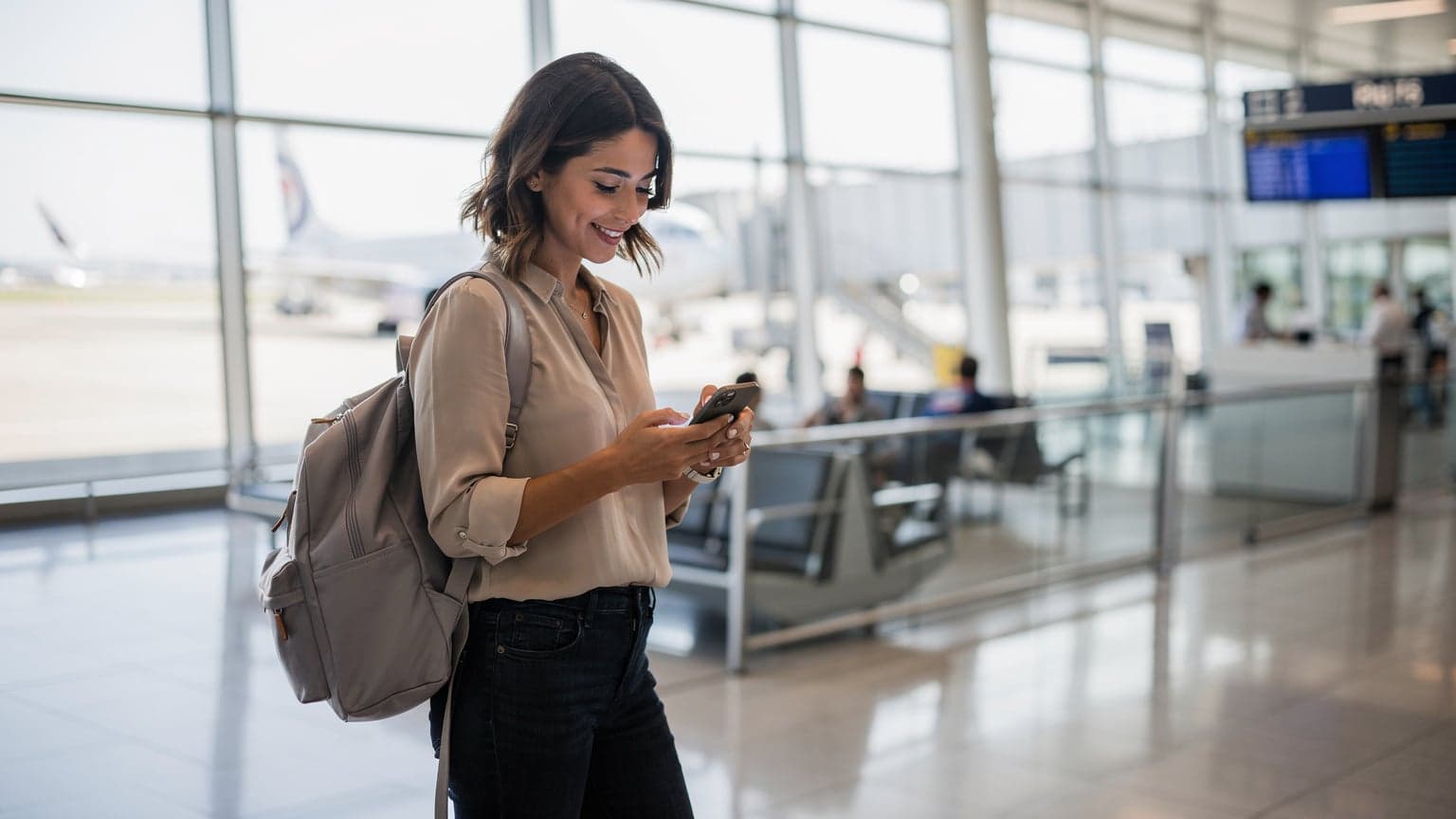 A woman at Charles de Gaulle Airport in Paris, France, confidently holding her new iPhone, having just transferred her eSIM and ready to connect.
