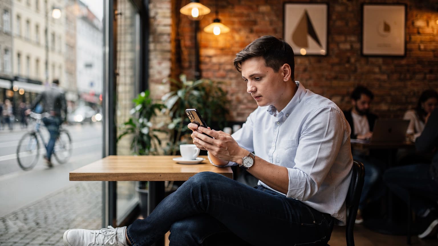 Eine Person sitzt an einem Tisch in einem Berliner Café, schaut auf ihr Smartphone und konfiguriert eine eSIM, während eine Tasse Kaffee daneben steht.
