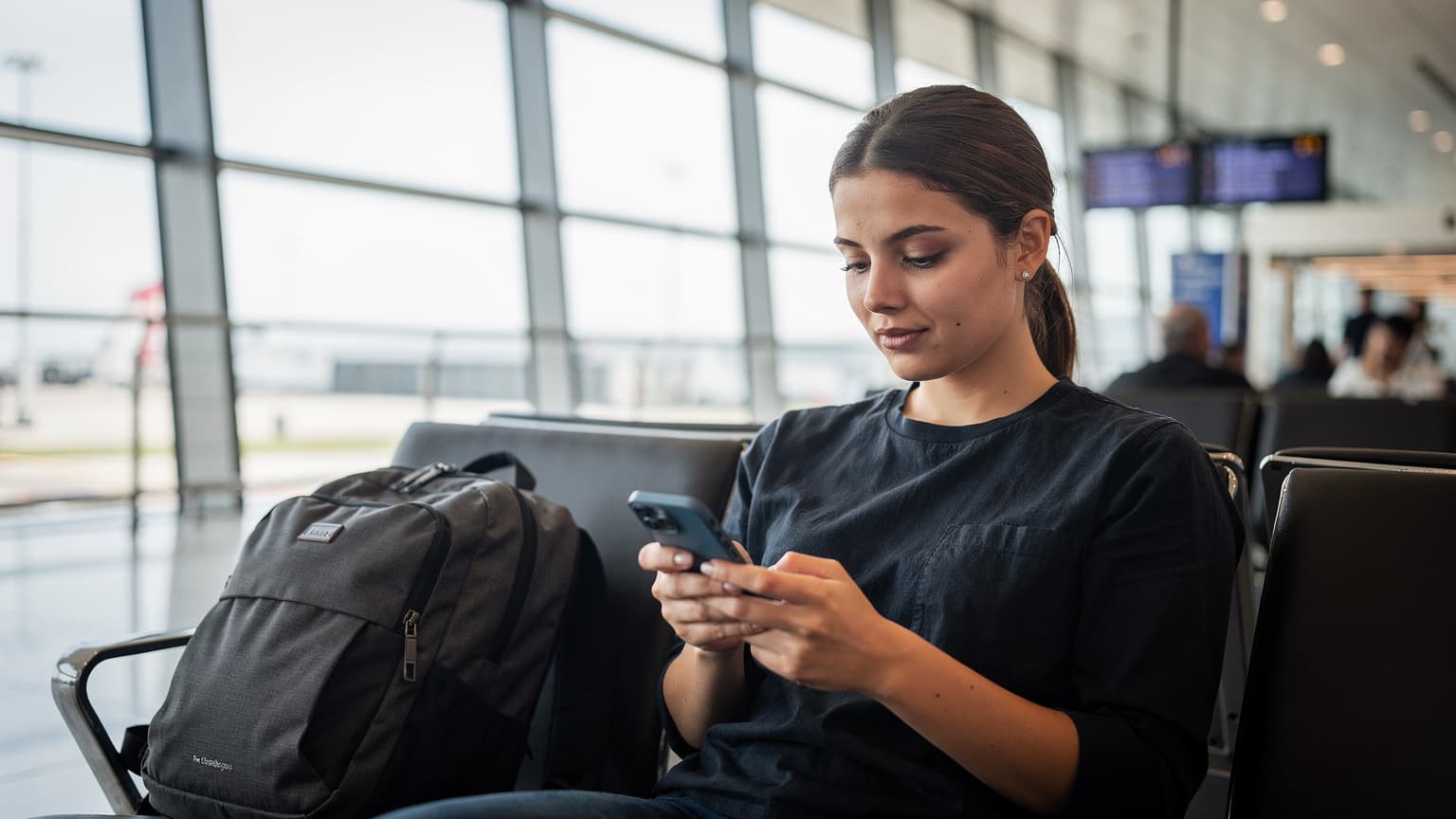 Une voyageuse navigue sur son iPhone à l'aéroport de Paris-Charles de Gaulle, vérifiant les détails de son eSIM avant un vol international.