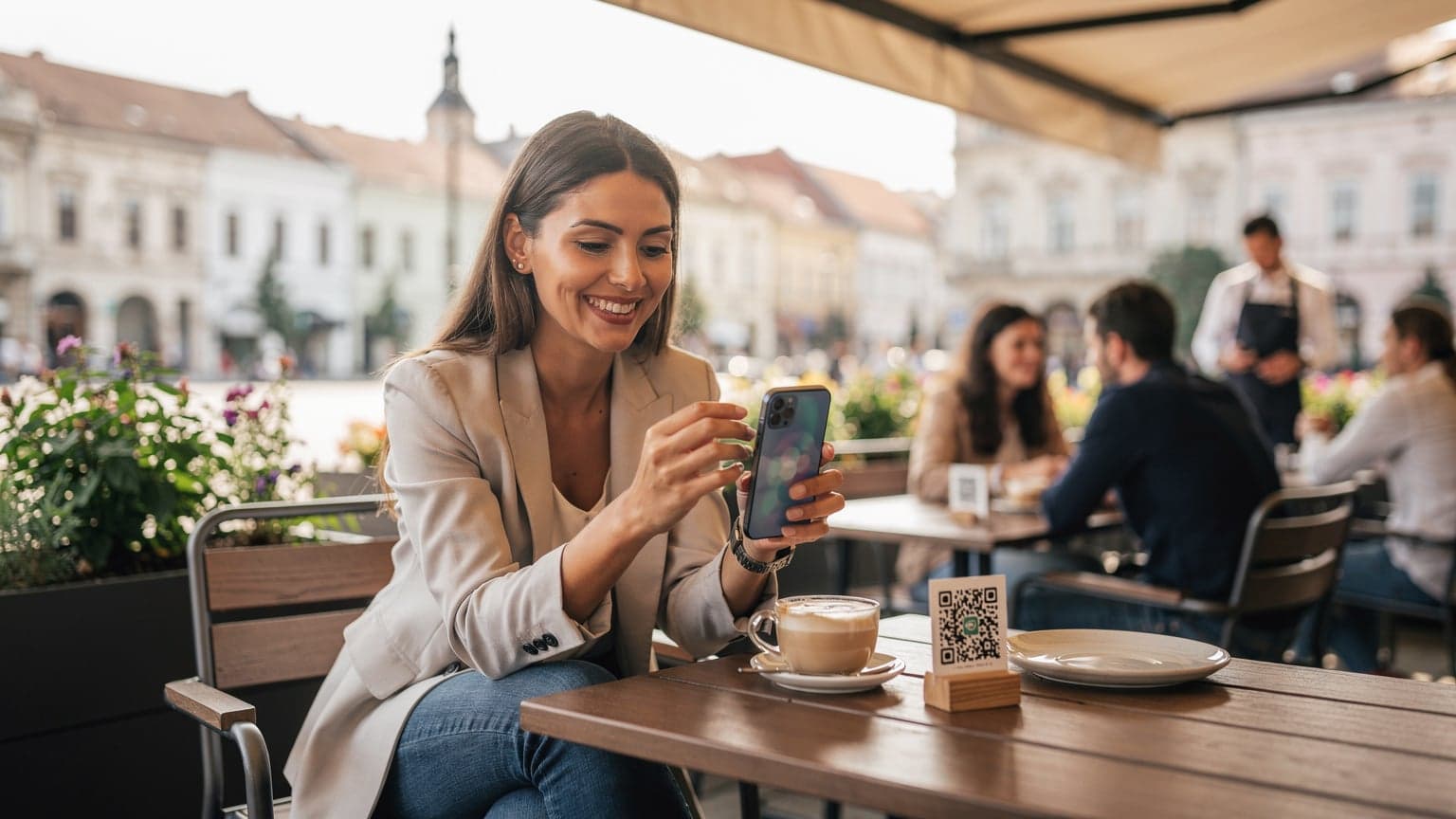 O femeie zâmbitoare, îmbrăcată casual, scanează un cod QR pentru activarea eSIM pe un iPhone, în timp ce stă la o terasă modernă în Piața Unirii din Cluj-Napoca, cu o cafea latte alături.