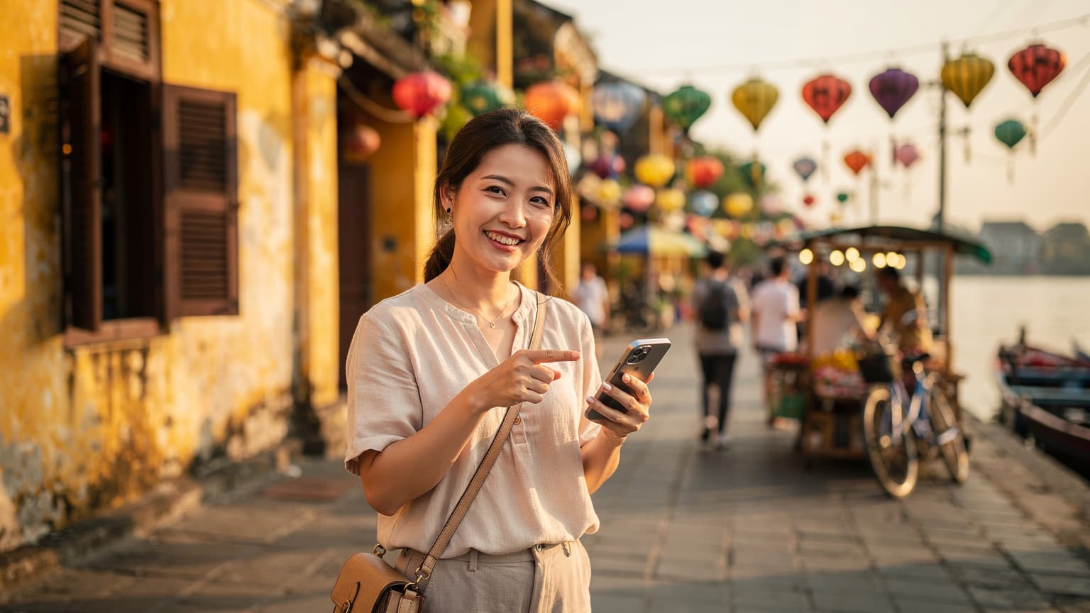ベトナムのホイアン旧市街で、スマートフォンの画面を指差しながら、笑顔で地図アプリを見ている日本人旅行者の女性。