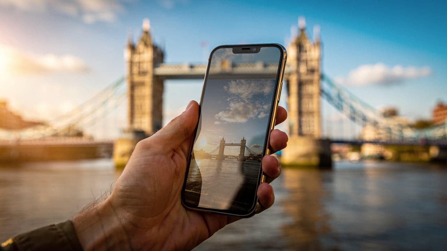 A close-up, cinematic shot of a hand holding a smartphone against a blurred background of London's iconic Tower Bridge at golden hour, symbolizing modern travel and digital connectivity.