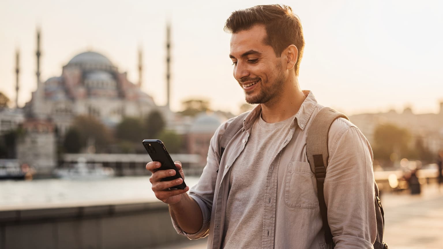 A person holds a smartphone in Istanbul, with a blurred view of an iconic landmark like the Hagia Sophia in the background, bathed in golden hour light. The image conveys modern travel and seamless digital connectivity.