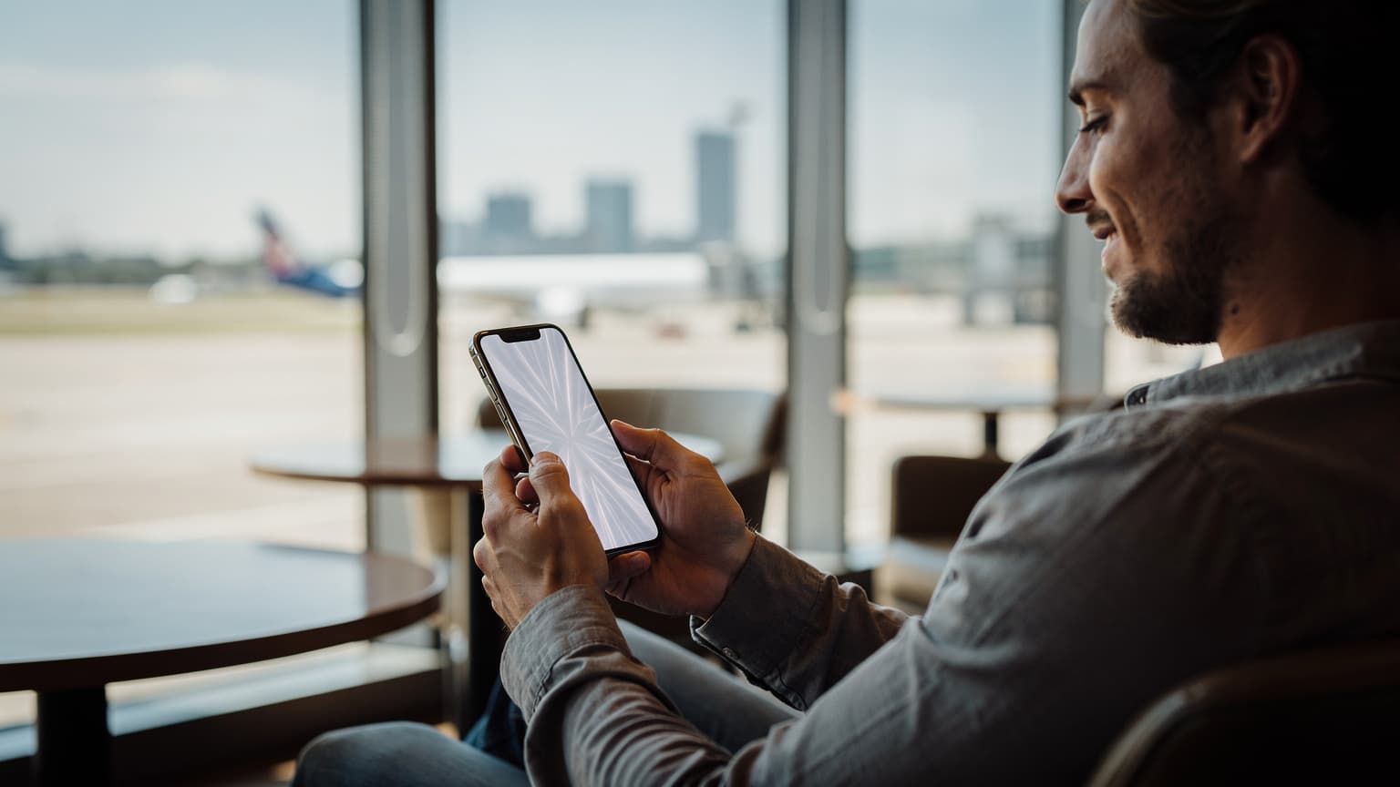 A person holding a modern iPhone in a bright, contemporary travel setting, looking at the screen with a relaxed expression, conveying easy and hassle-free mobile connectivity while traveling.