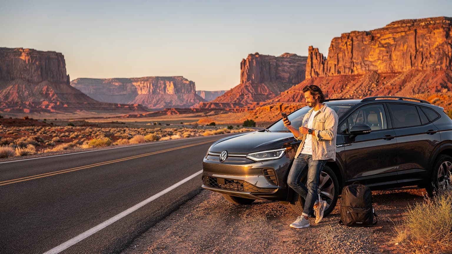 A person uses a smartphone beside an SUV on a scenic desert road in the American West, with red rock formations in the background, implying seamless travel connectivity and data usage.