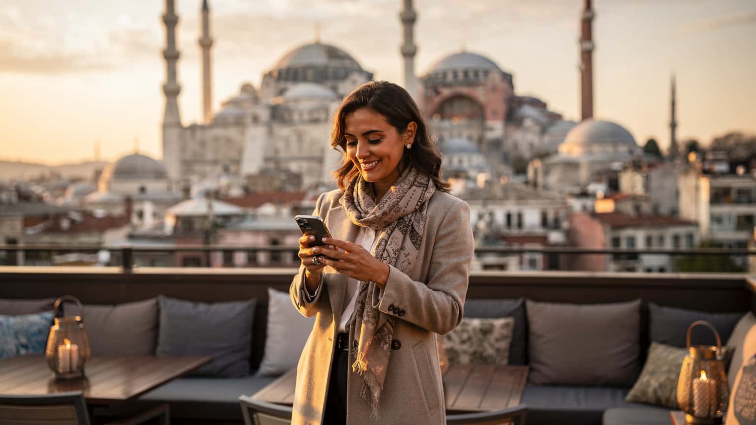 Une femme souriante tenant son téléphone avec une vue panoramique sur les toits d'Istanbul et la Mosquée Bleue au coucher du soleil en arrière-plan.