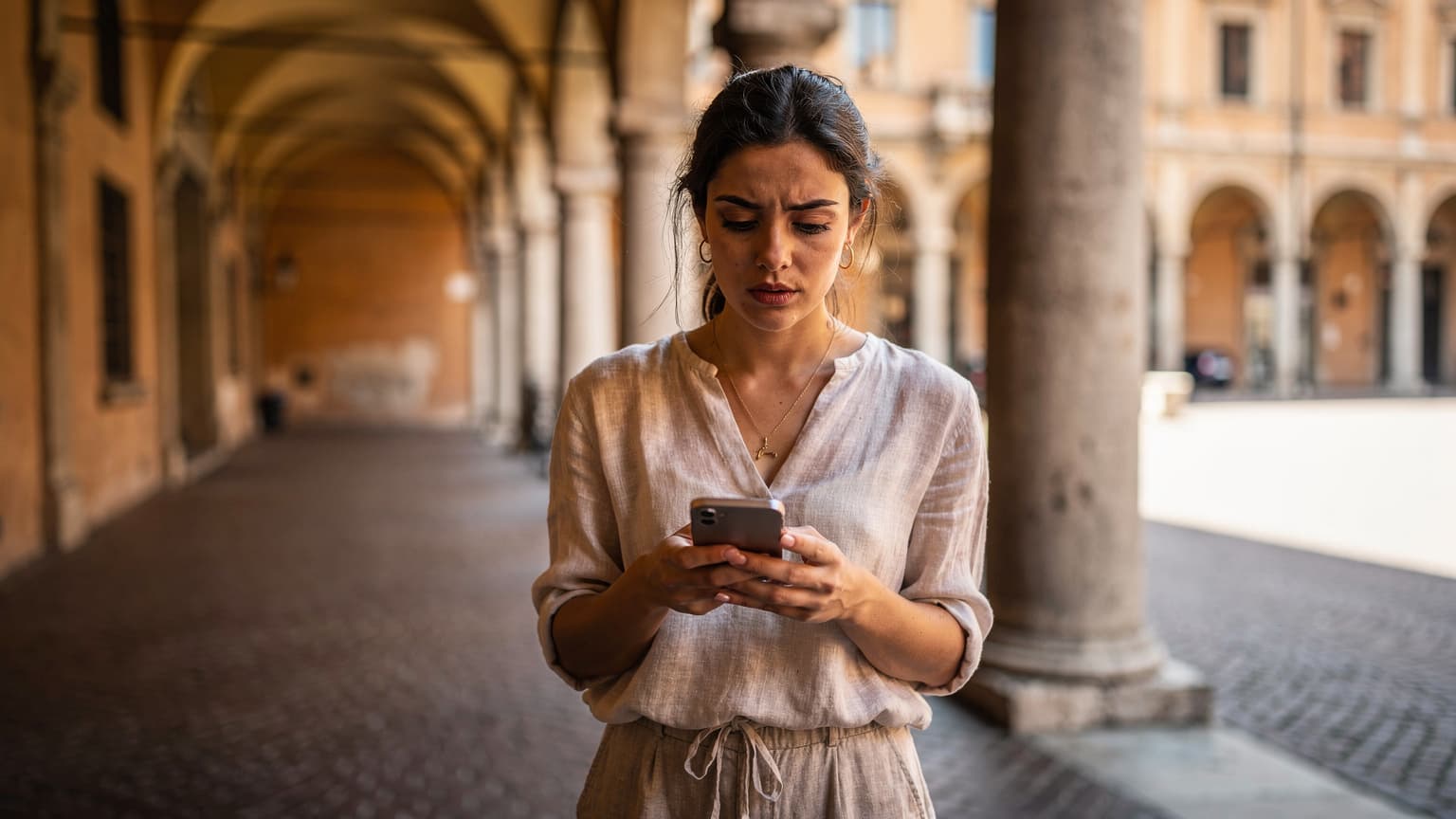 Een reiziger bekijkt de route op haar telefoon terwijl ze verkoeling zoekt in de schaduw van een historische arcade in Bologna, Italië.