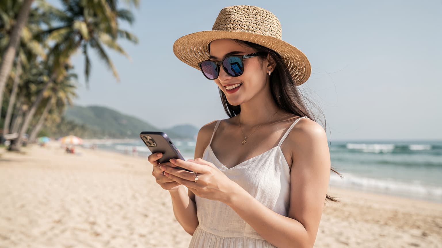 Một phụ nữ Việt Nam trẻ tuổi, đeo kính râm và mũ cói, đang mỉm cười và lướt điện thoại thông minh trên bãi biển Mỹ Khê, Đà Nẵng, với những hàng dừa và biển xanh phía sau.