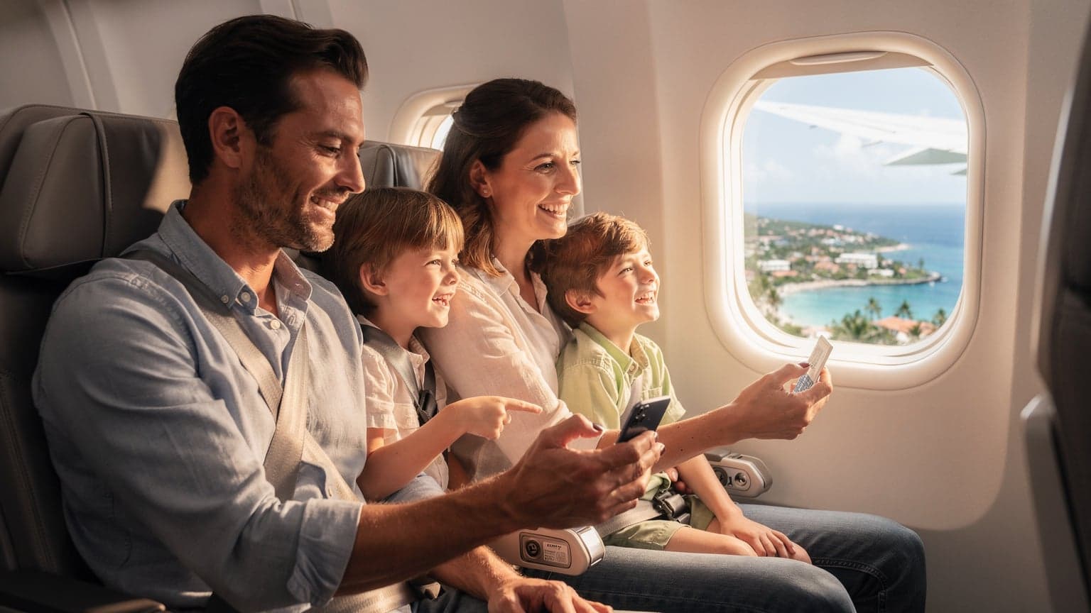 Een gezin, bestaande uit twee ouders en twee kinderen van 8 en 10 jaar, lachend terwijl ze vanuit een vliegtuigraam kijken naar de landing op een zonnige bestemming, met een smartphone in de hand van de vader die een eSIM QR-code scant.