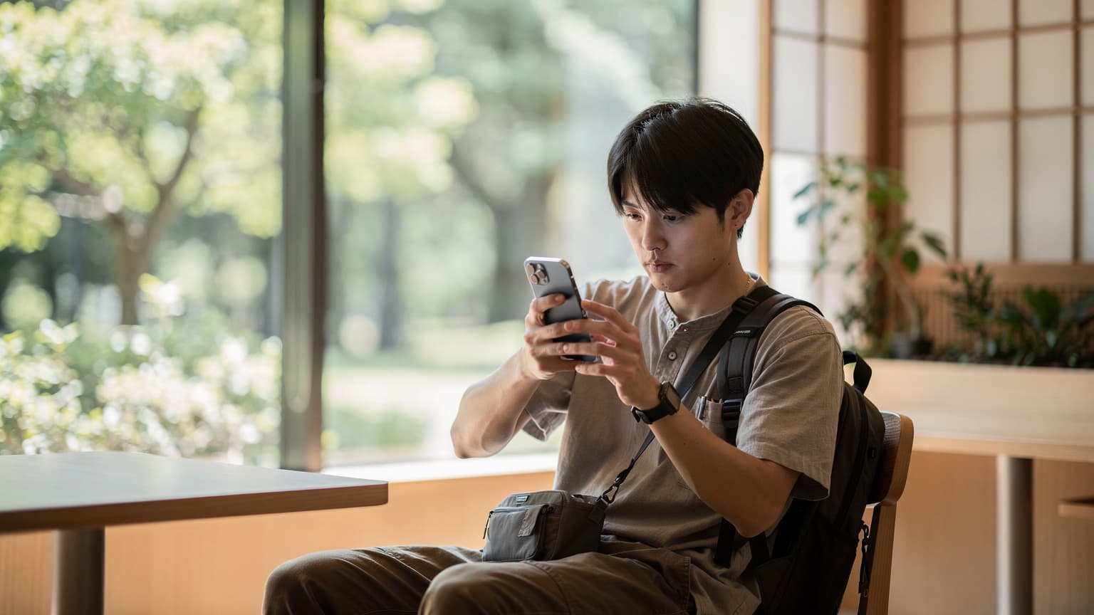 東京の新宿御苑近くのカフェで、iPhone 17を使って海外eSIMの設定を最終確認している若い男性旅行者。