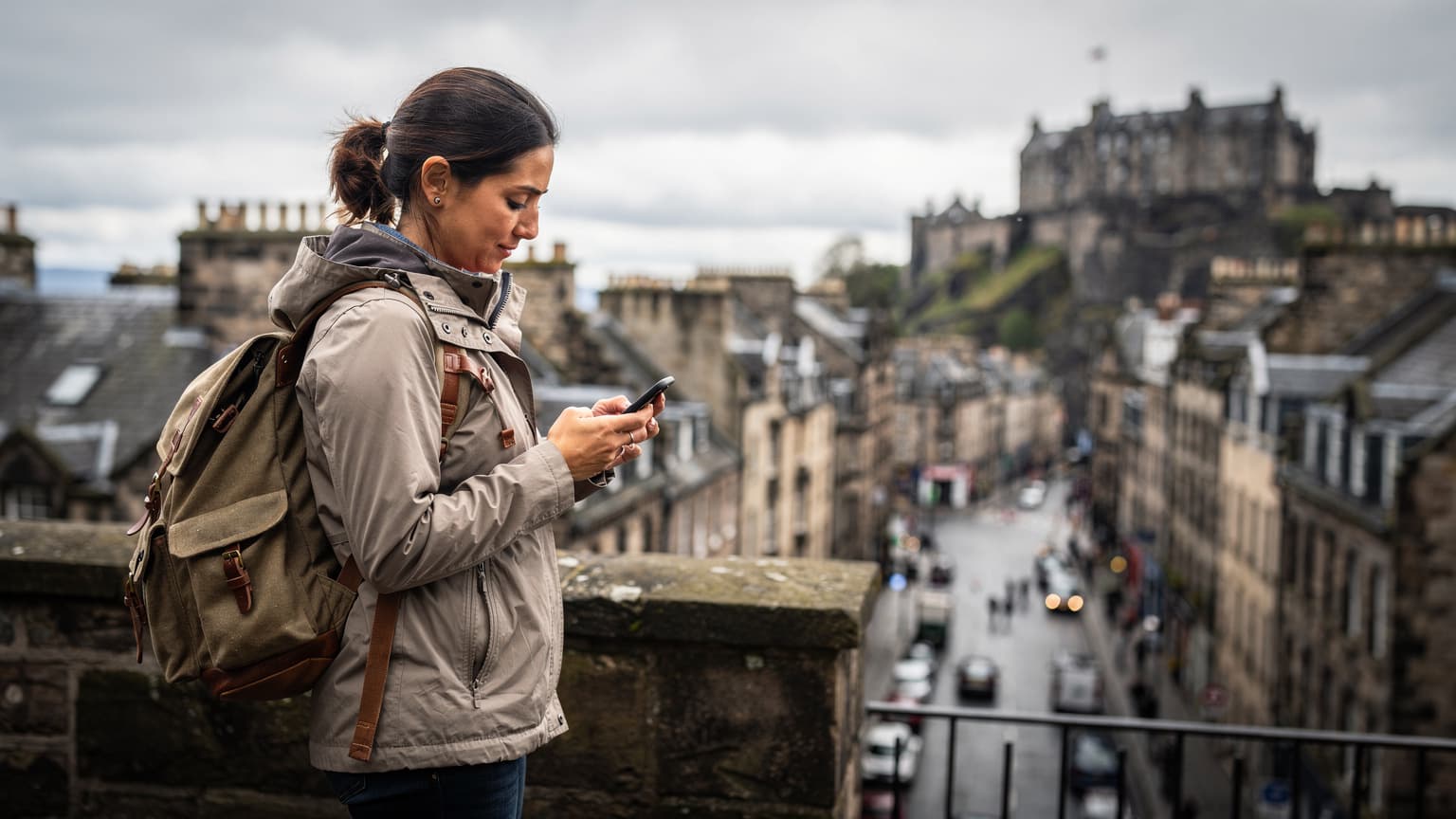 Una viajera activa en el centro de Edimburgo, usando su teléfono para consultar un mapa digital con el Castillo de Edimburgo de fondo.
