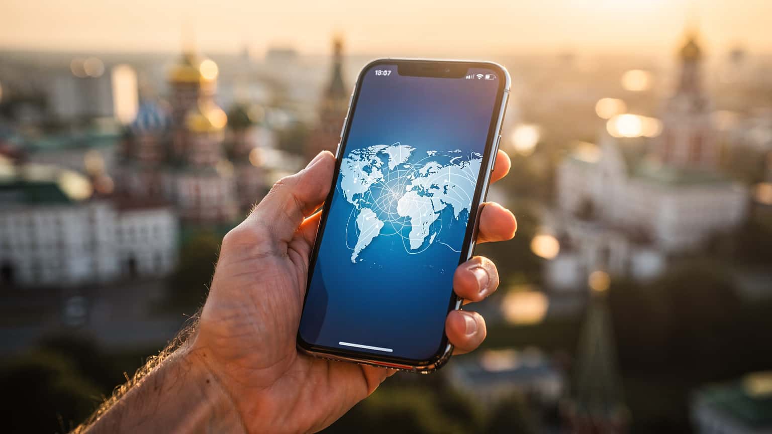 A close-up of a hand holding a smartphone with a bright screen, set against a blurred background of a modern Russian city or landscape, symbolizing global connectivity and travel.