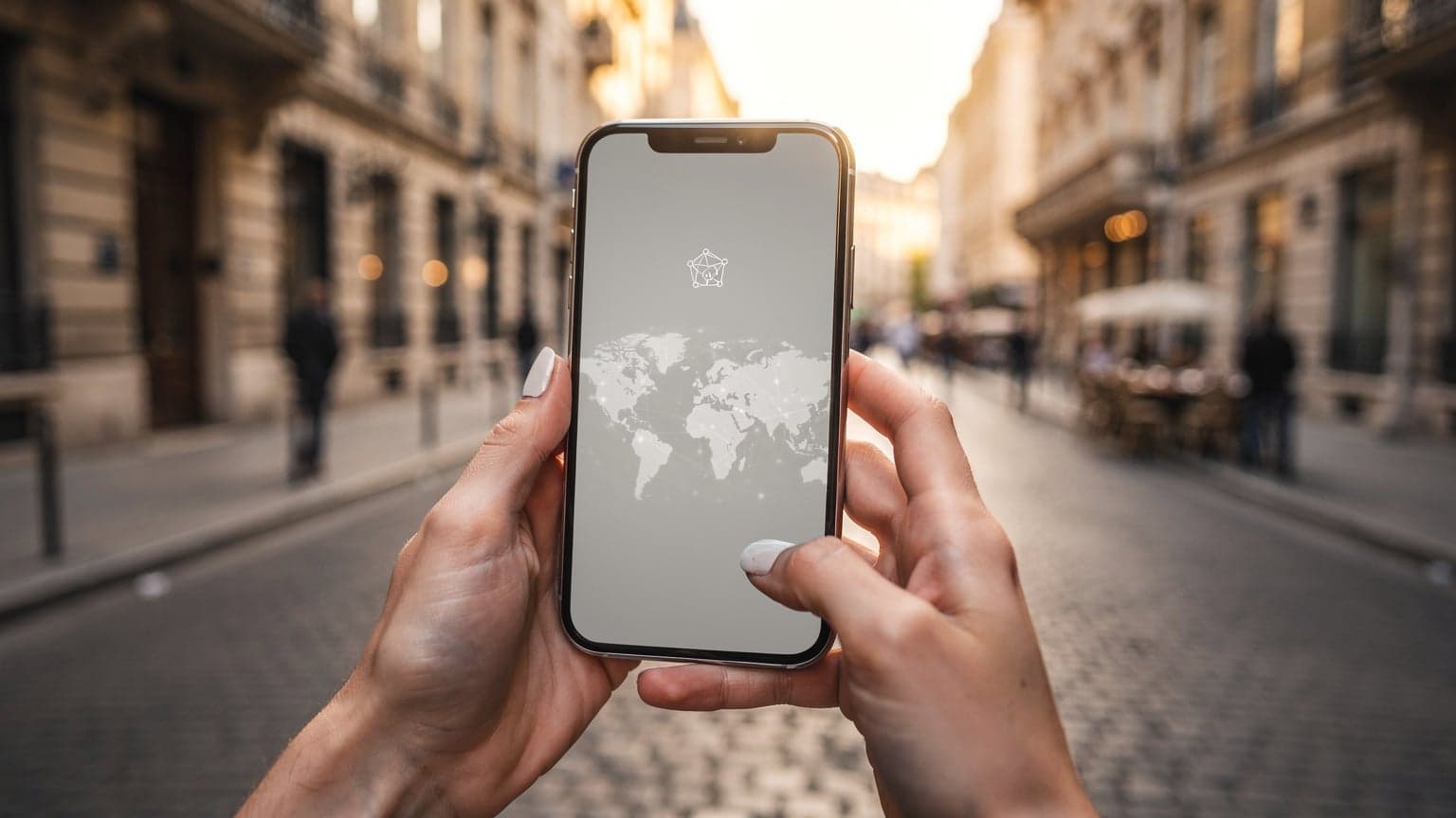 A close-up of hands holding a smartphone, with a softly blurred background showing a vibrant European city street. The image conveys modern travel and seamless digital connectivity, suitable for a travel tech magazine.
