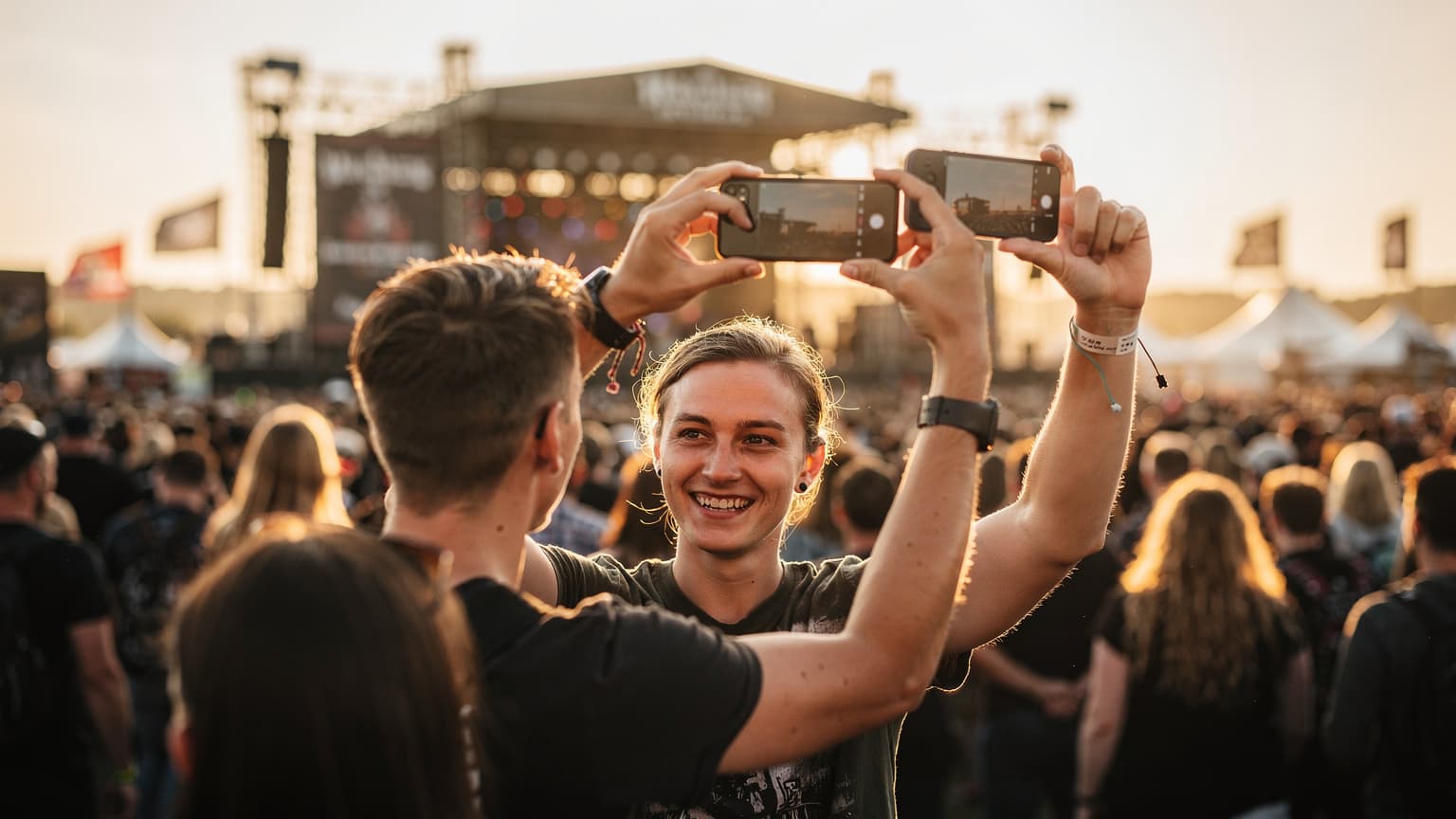 Ein junger Festivalbesucher, der bei Sonnenuntergang inmitten einer feiernden Menschenmenge sein Smartphone hochhält, während er ein Foto macht.