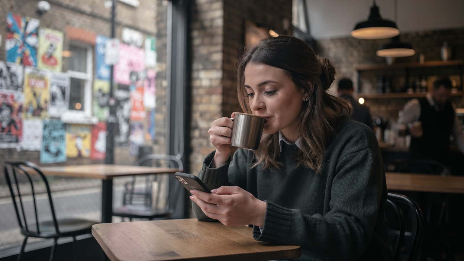 Londra'nın Shoreditch semtinde, bir kafenin penceresinden dışarıyı izleyen bir kadın, elinde kahve bardağıyla telefonuna bakıyor.