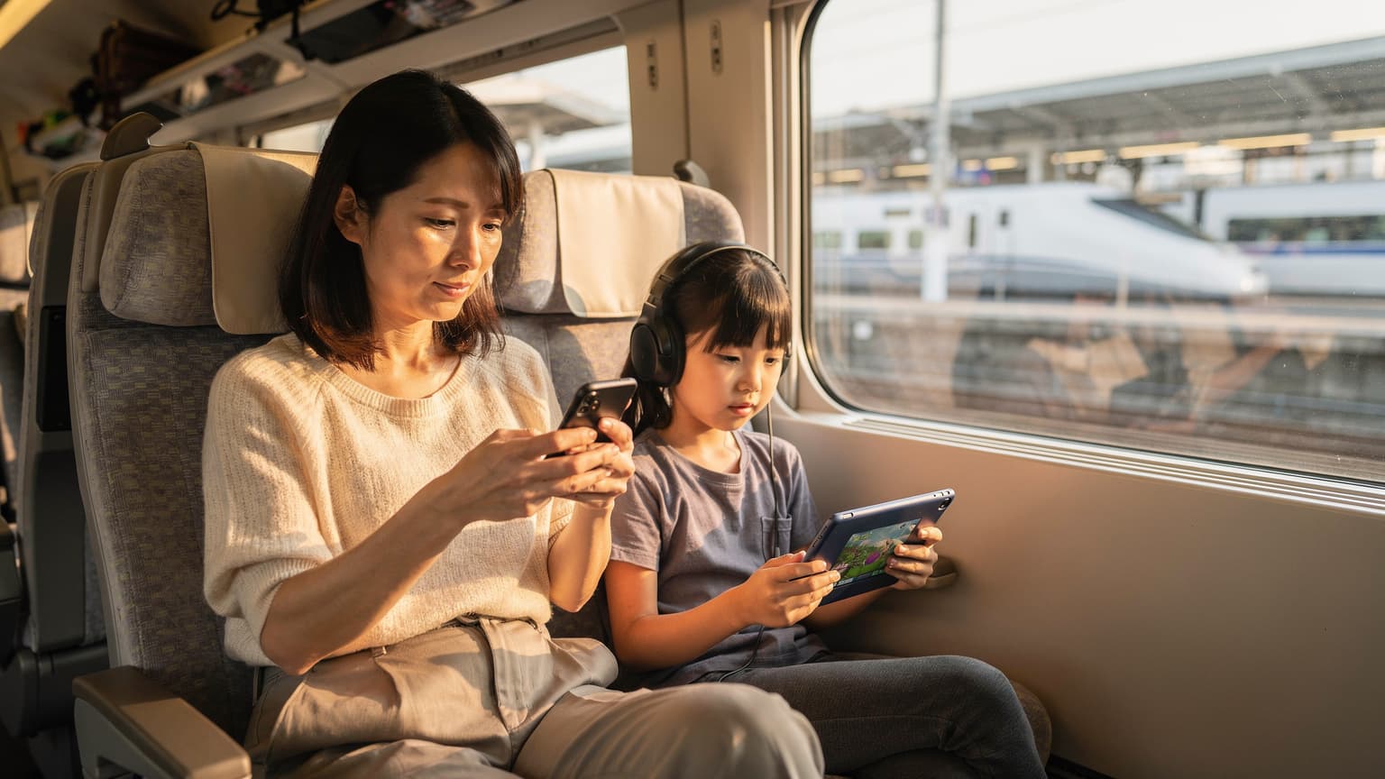 東京駅の新幹線ホームで、母親が子供が座っている隣でiPhoneのeSIM設定画面を確認している様子。窓の外には新幹線が停車している。