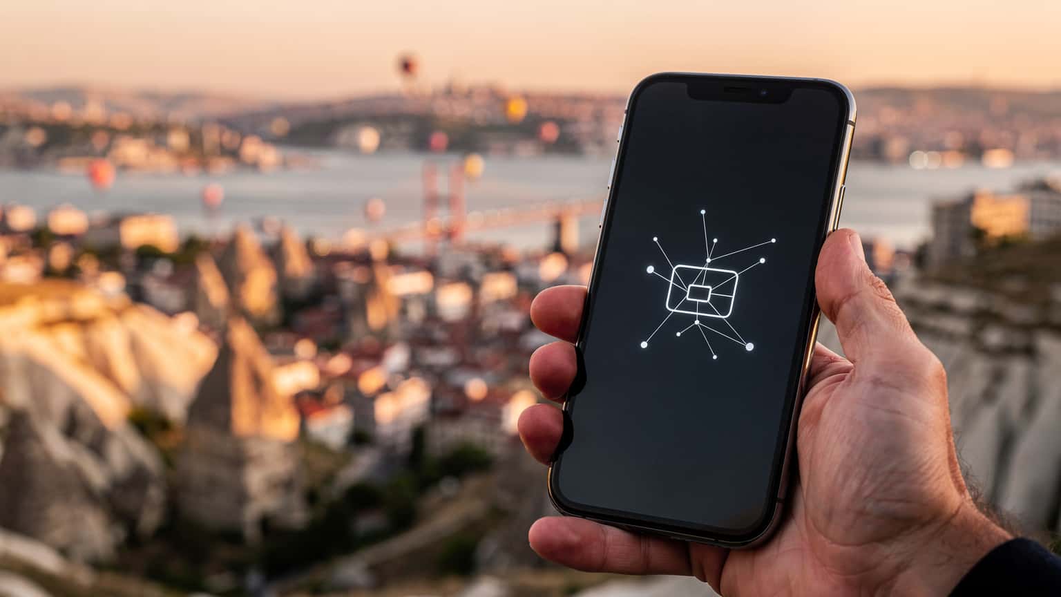 A hand holding a smartphone displaying a digital network symbol, set against a blurred, scenic Turkish travel background, illustrating modern connectivity for travelers.